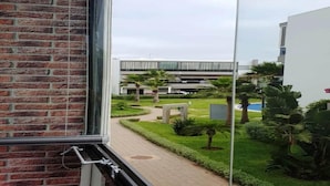 A view from a window of a brick building with a pathway leading to a modern building with a pool. - Pleasant Apartment in Blanca Beach 4873 (Sidi Rahal)