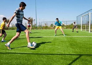 Eine Gruppe von Menschen spielt Fußball auf einem grünen Feld, im Hintergrund ist ein Tor zu sehen.