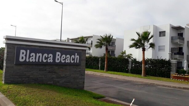 A sign for 'Blanca Beach' with modern buildings in the background. - Pleasant Apartment in Blanca Beach 4873 (Sidi Rahal)