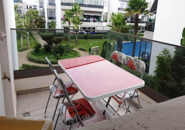 Ein Balkon mit Tisch und Stühlen mit Blick auf einen Pool und Grünflächen.