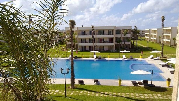 A hotel with a large pool, multiple balconies, and palm trees. - Pleasant apartment in Ola Blanca 4876 (Sidi Rahal)
