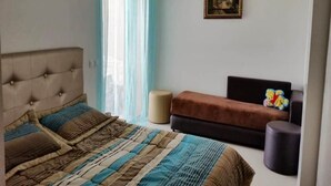 A bedroom with a bed, a sofa, a small round table, and a wall-mounted picture. - Pleasant apartment in Ola Blanca 4876 (Sidi Rahal)