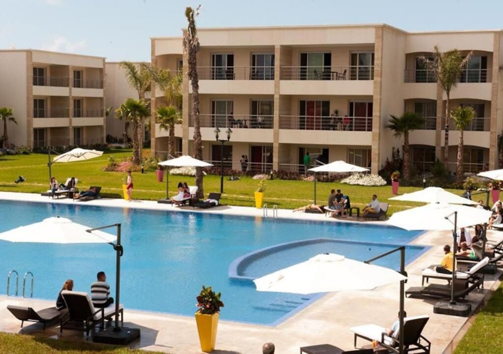 Un hotel con piscina, mobiliario exterior y palmeras.