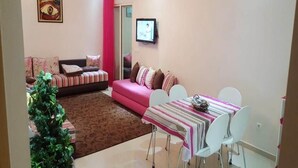 A living room with a pink sofa, a dining table with a striped tablecloth, and a small Christmas tree. - Pleasant apartment in Ola Blanca 4876 (Sidi Rahal)