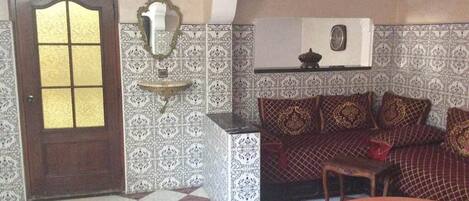 Una habitación con piso a cuadros, paredes estampadas, una puerta de madera con paneles de vidrio, un sofá con cojines decorados y una mesita.