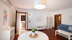 Una sala de estar moderna con una mesa redonda blanca, un sofá azul y una lámpara en el techo.
