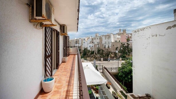 Un balcón con vista a un paisaje urbano, una maceta blanca y una reja de metal.