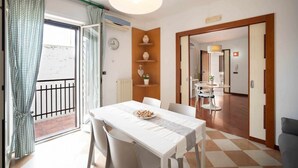 Un comedor con una mesa lista para dos personas, un reloj en la pared y vistas al balcón.