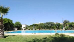 Une piscine entourée de verdure, avec un bâtiment blanc en arrière-plan.