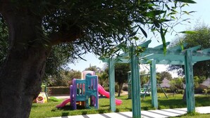 Un terrain de jeux avec des toboggans et des structures d’escalade, entouré d’herbe et d’arbres.