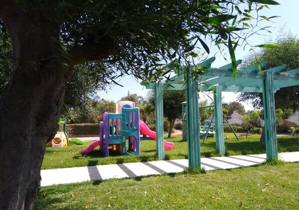 Un parque infantil con toboganes y estructuras para escalar, rodeado de césped y árboles.