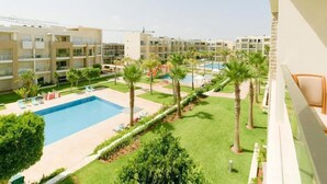 Une cour d’hôtel avec une piscine, des palmiers et une vue sur les bâtiments adjacents.