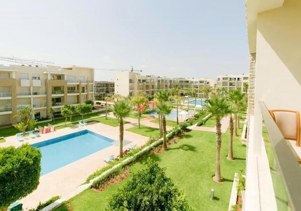 Un patio de hotel con piscina, palmeras y vistas a edificios colindantes.