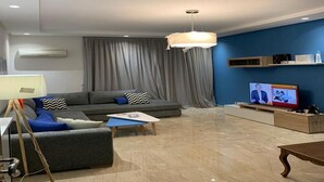 Ett modernt vardagsrum med en grå soffa, ett soffbord, en tv på ett tv-bord och en blå vägg.