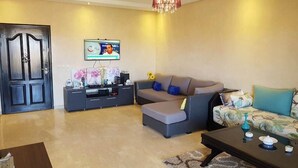 A living room with a sofa, a coffee table, a TV, and a chandelier.