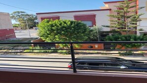 Ein Balkon mit Blick auf ein Wohngebiet, darunter eine Straße mit einem Auto und Gebäude mit roten und weißen Fassaden.
