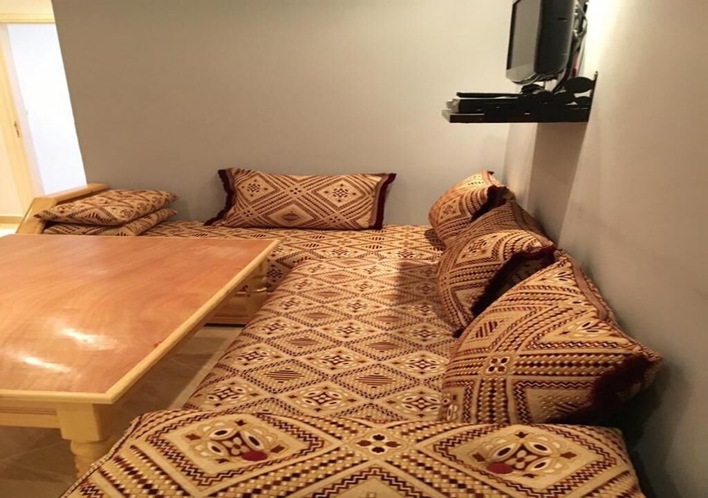 A cozy room with a wooden dining table, patterned sofa, and a flat-screen TV mounted on the wall.