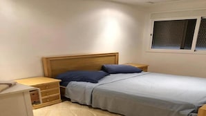 A bedroom with a bed, wooden headboard, bedside tables, and a window with blinds. - Beautiful apartment in Saidia 4895 (Saidia)