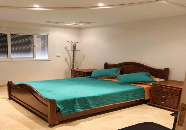 A neatly made bed with a teal bedspread, a wooden headboard, and a nightstand with drawers.