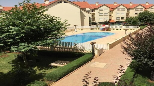 A hotel with a swimming pool, a white picket fence, and a well-maintained lawn.