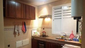 A kitchen with wooden cabinets, a stove, a sink, and a window with blinds.
