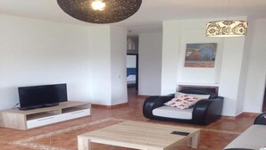 A modern living room with a flat-screen TV, a leather armchair, a coffee table, and a patterned rug. - Superb Villa in Marina Saidia 4899 (Saidia)