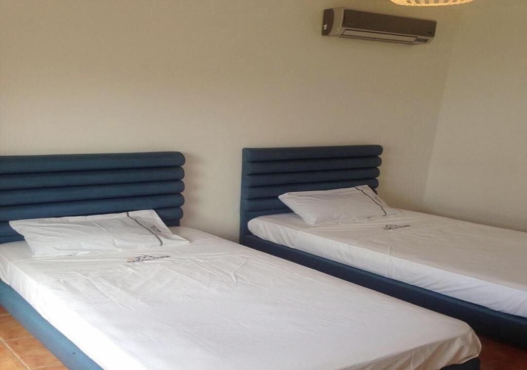 Two single beds with blue headboards in a room with a white wall and an air conditioning unit above.