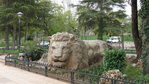 A large stone lion statue in a park with a paved walkway and metal railing. - Beautiful apartment in Ifrane 4902 (Ifrane)