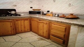 A kitchen with wooden cabinets, a microwave, a stove, and a tiled floor. - Beautiful apartment in Ifrane 4902 (Ifrane)
