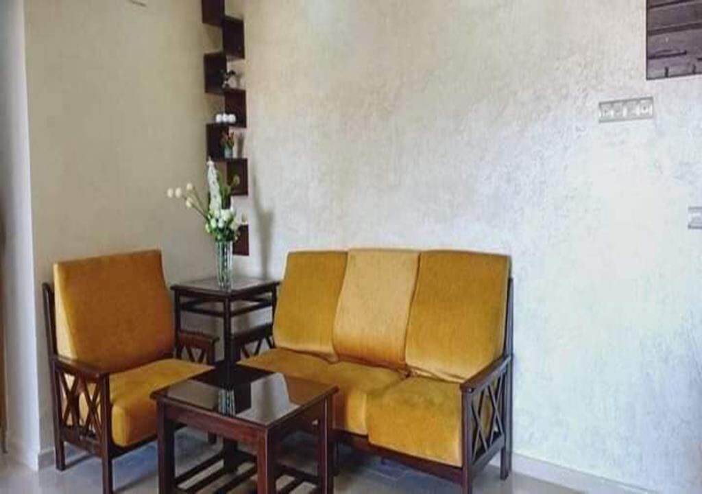 Ein Wohnzimmer mit einer Couch, zwei Sesseln, einem Couchtisch und einem kleinen Beistelltisch mit Blumen in einer Vase.