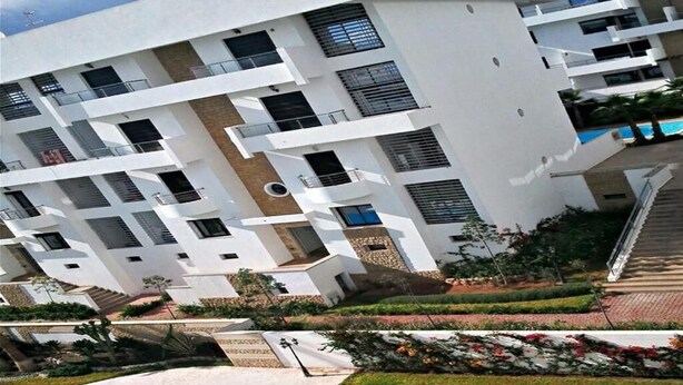 Un immeuble à plusieurs étages doté de balcons, d’une piscine et de jardins aménagés.