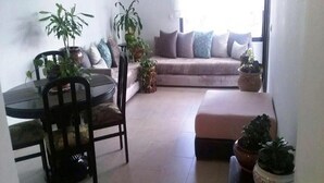 Un salon avec une table ronde en verre, un canapé et plusieurs plantes en pot.