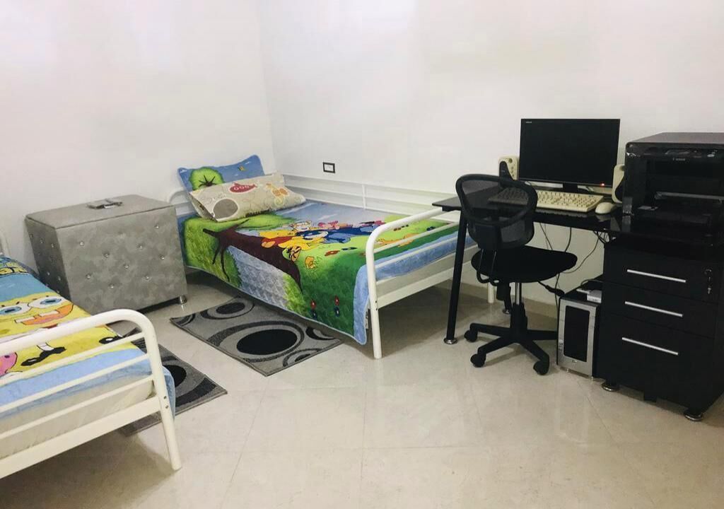 Un dormitorio con una cama, un escritorio con una computadora, una impresora y un archivador.