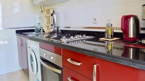Una cocina moderna con electrodomésticos de acero inoxidable, lavadora integrada y armarios rojos.