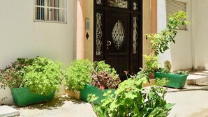 A house with a black ornate door, a small window with bars, and several green planters with various plants. - Pleasant sea view apartment El Hamra II 4919 (Asilah)