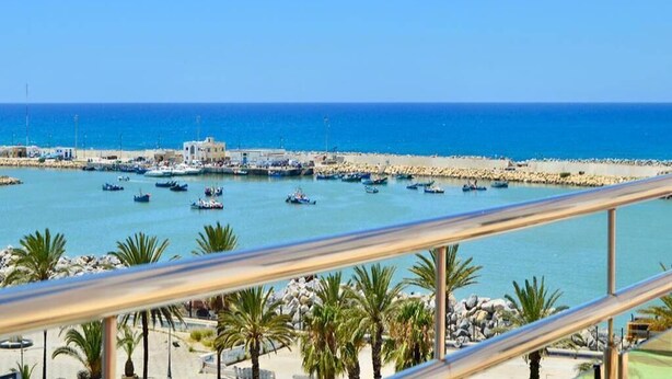 A coastal marina with boats, a rocky breakwater, and palm trees. - Pleasant sea view apartment El Hamra II 4919 (Asilah)