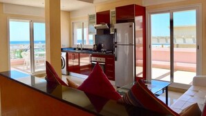 A modern kitchen with red cabinets, a stainless steel refrigerator, and a large window overlooking a balcony. - Pleasant sea view apartment El Hamra II 4919 (Asilah)