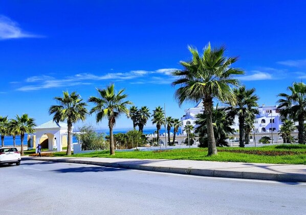 A coastal street lined with palm trees and buildings with Mediterranean architecture. - Al Amine Beach Complex Fnideq 4928 (Fnideq)