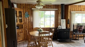 A dining area with a wooden table and chairs, a ceiling fan, and a view of the outdoors through a large window.