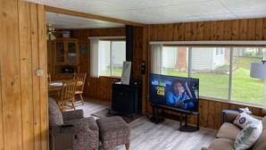 A cozy living room with wooden walls, a TV, a dining area, and large windows.
