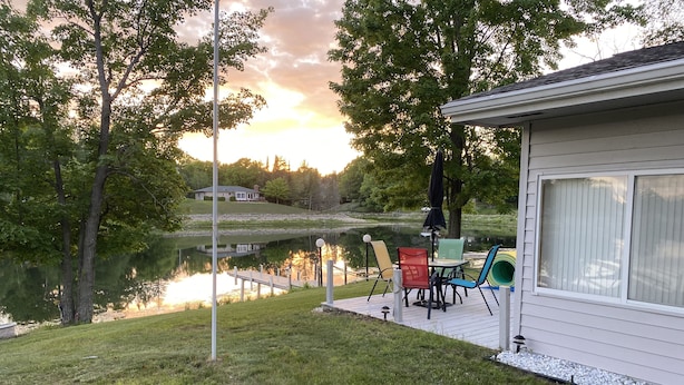 A lakeside patio with a table and chairs, a deck, and a house in the background.