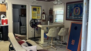 A compact living space with a bed, a dining area with a table and chairs, a fan, and a refrigerator.