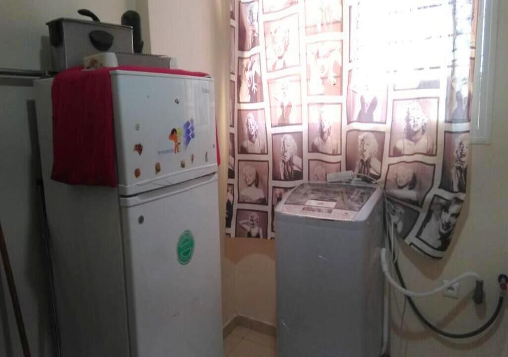 Une cuisine compacte équipée d’un réfrigérateur, d’un lave-linge et d’un mur décoré de tableaux encadrés.