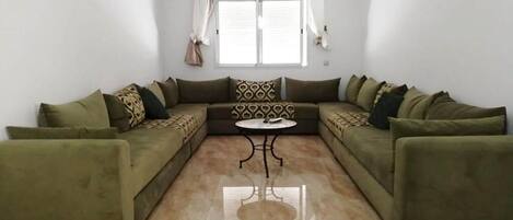 Una sala de estar con un sofá modular, una mesita redonda y un ventanal con cortinas.