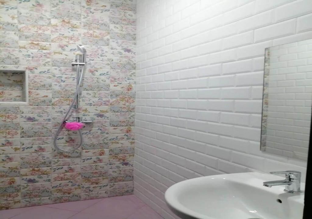Een badkamer met tegels met een bloemmotief, een witte wastafel en een douche met een handdouche.