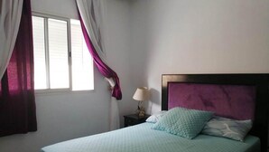 Un dormitorio con una cama, una mesita de noche, una ventana con cortinas y una lámpara de pared.