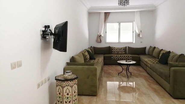 Una sala de estar con un sofá seccional, una mesa redonda pequeña y un televisor montado en la pared.