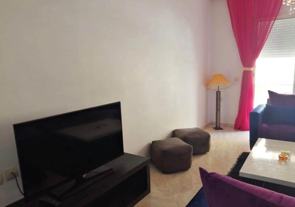 A living room with a flat-screen TV, two ottomans, a lamp, and a sofa.