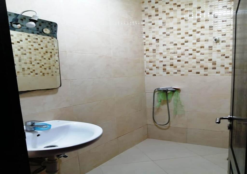 A bathroom with a sink, a shower with a green hose, and a tiled wall with a mosaic pattern.