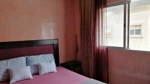 A bedroom with a bed, a nightstand, and a window with curtains. - Residence Jawharat Mogador 4938 (Essaouira)